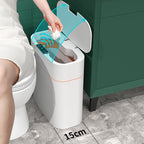 A white smart trash can with a hinged lid is shown next to a toilet in a bathroom setting. A hand is placing a tissue into the open bin, with blue graphic arrows indicating the lid opening motion and a '15cm' size marker on the floor showing the bin's width.