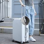 Person pulling a white suitcase with a cat carrier on top outdoors.